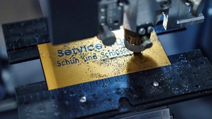 Bronzenes Schild wird mit Aufschrift "Servicepunkt-Bremen, Schuh- und Schlüsseldienst" unter einer Gravurmaschine graviert.